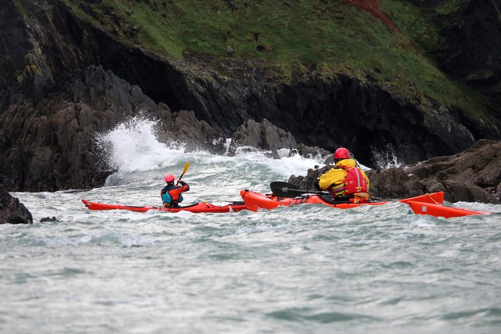 Two experienced sea kayakers paddling through rough water beside the Pembrokeshire coast